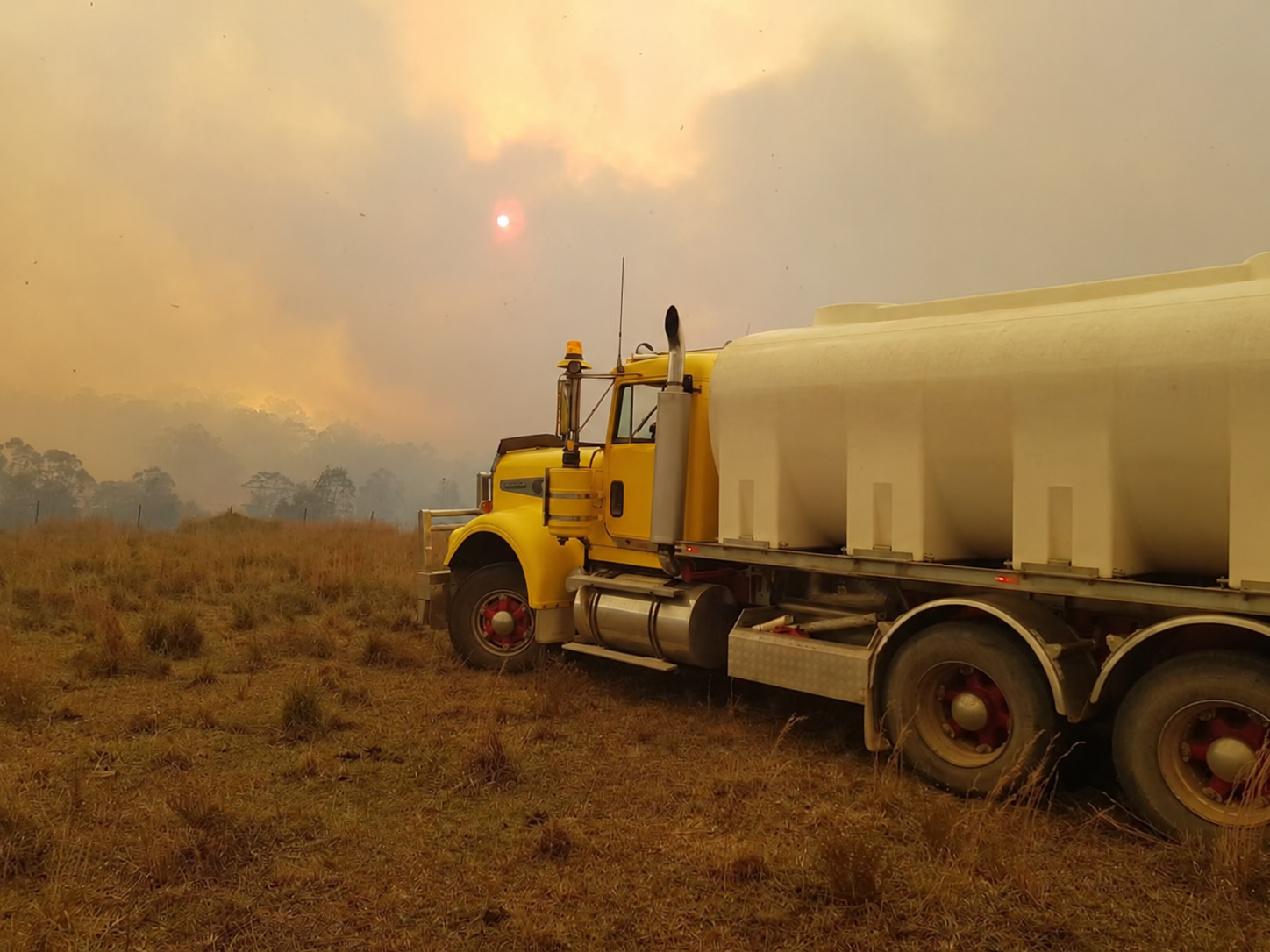 Yellow Water Truck on a Smoky Dirt Road Near Grassland — Taree & Mid Coast Water Cartage in Hillville, NSW