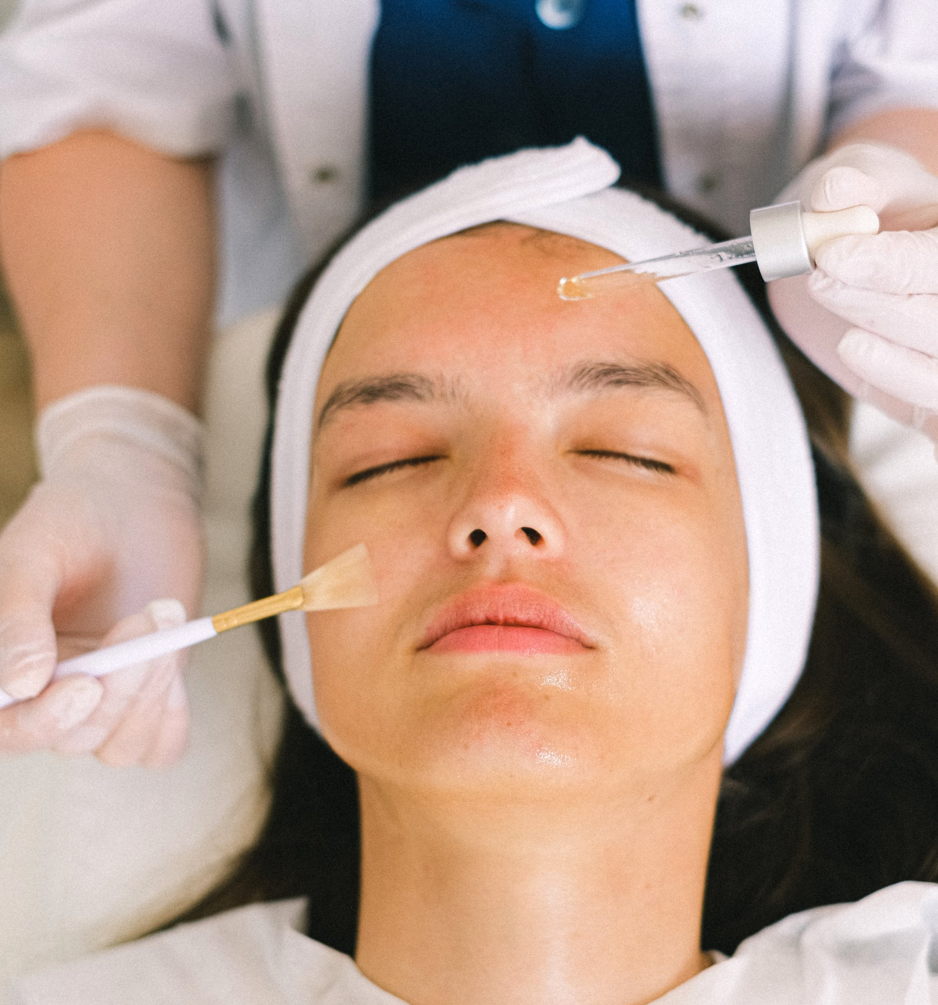 Persoon die een gezichtsbehandeling ondergaat: serum aanbrengen en exfoliëren.