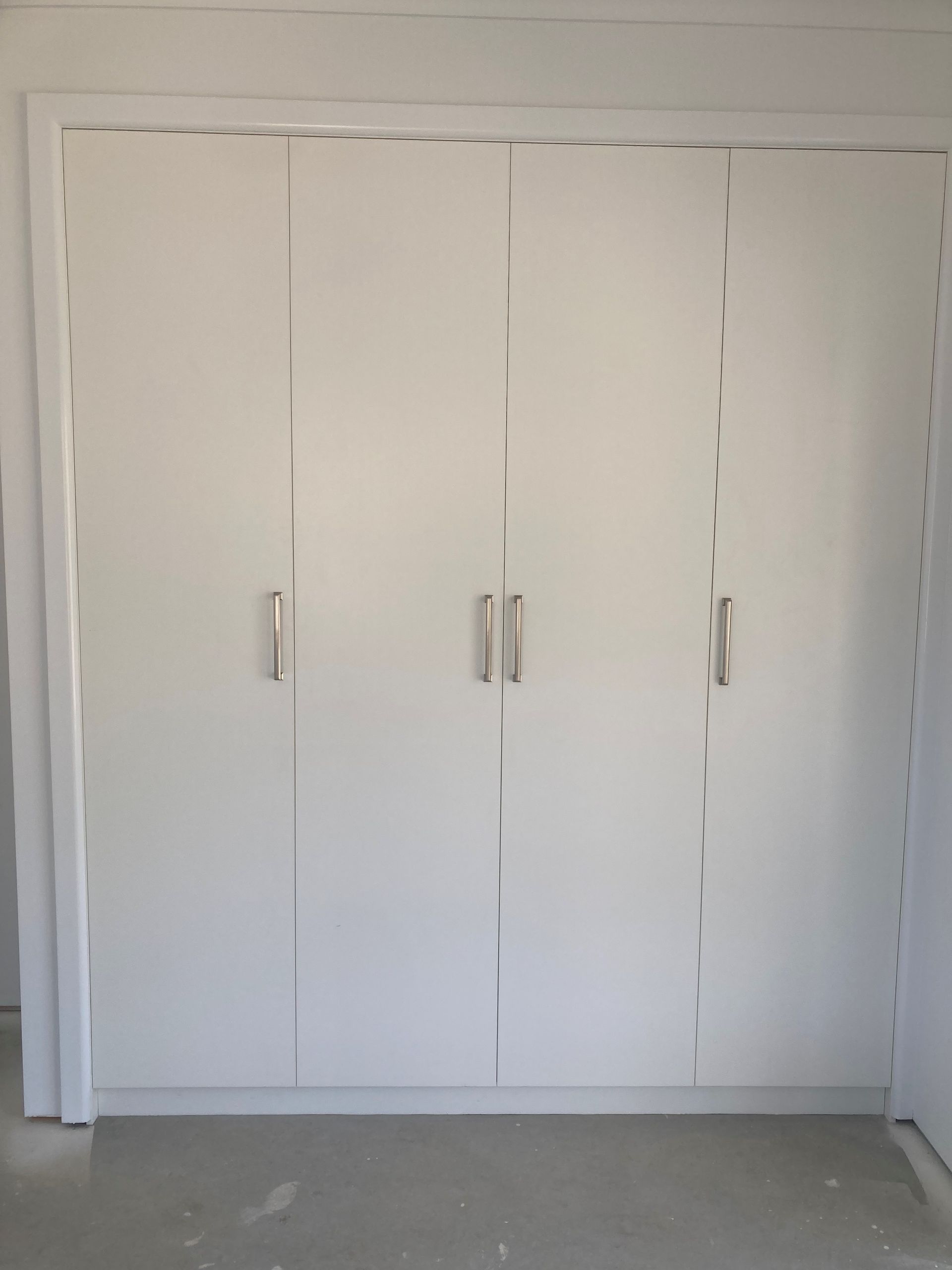 White Built-in Closet With Four Doors and Silver Handles in a Plain Room — Valley Cabinetmakers Pty Ltd In Biloela, QLD