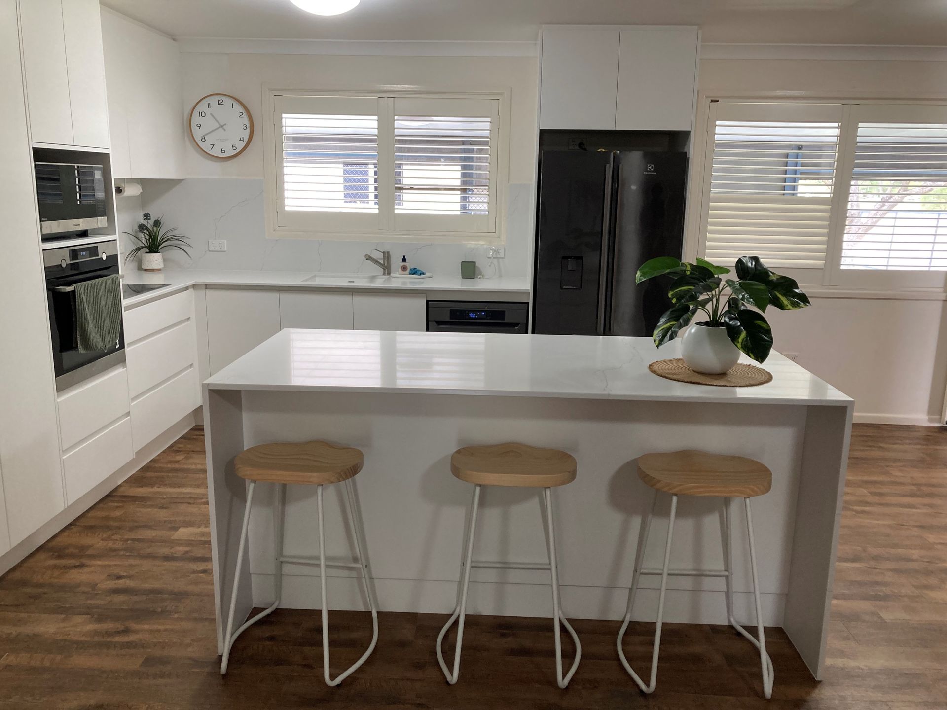 Bright White Kitchen, Three Stools, Black Fridge, Wall Clock, and Plant — Valley Cabinetmakers Pty Ltd In Biloela, QLD
