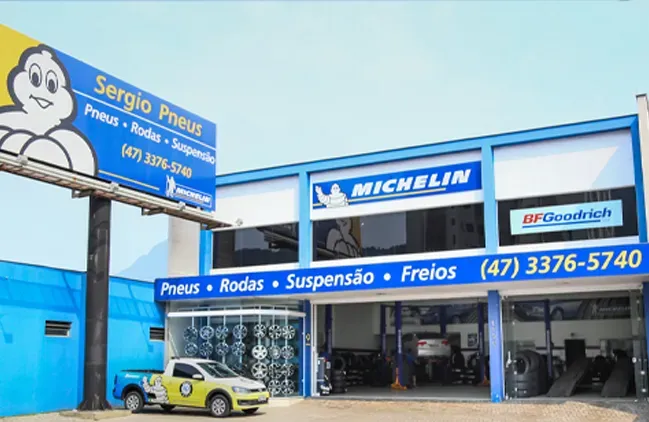 Oficina mecânica Michelin com fachada azul, carro amarelo e placa em português na rua.
