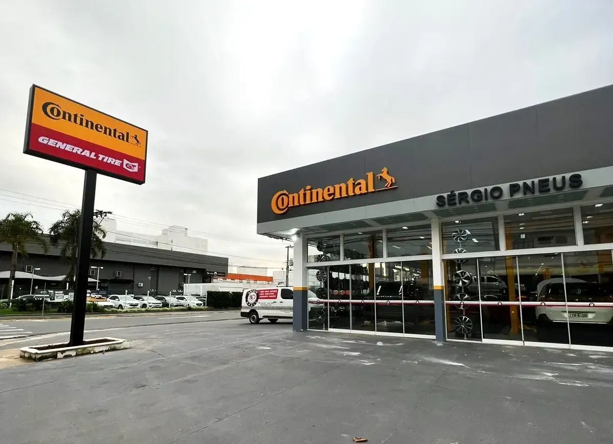 Fachada da loja de pneus Continental com vitrine de vidro e placa na beira da estrada sob céu nublado.