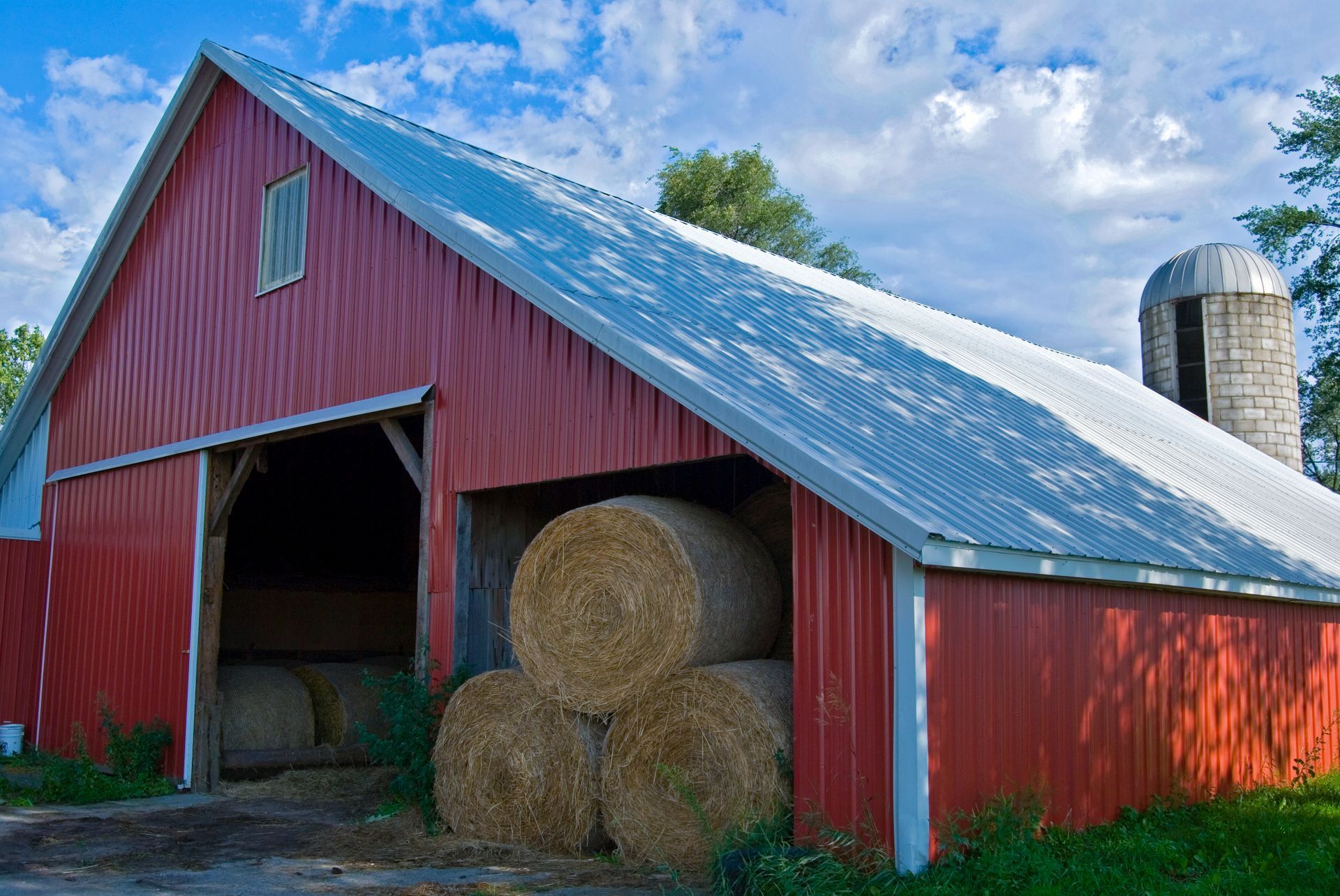 A red barn filled with hay bales and a silo in the background.
