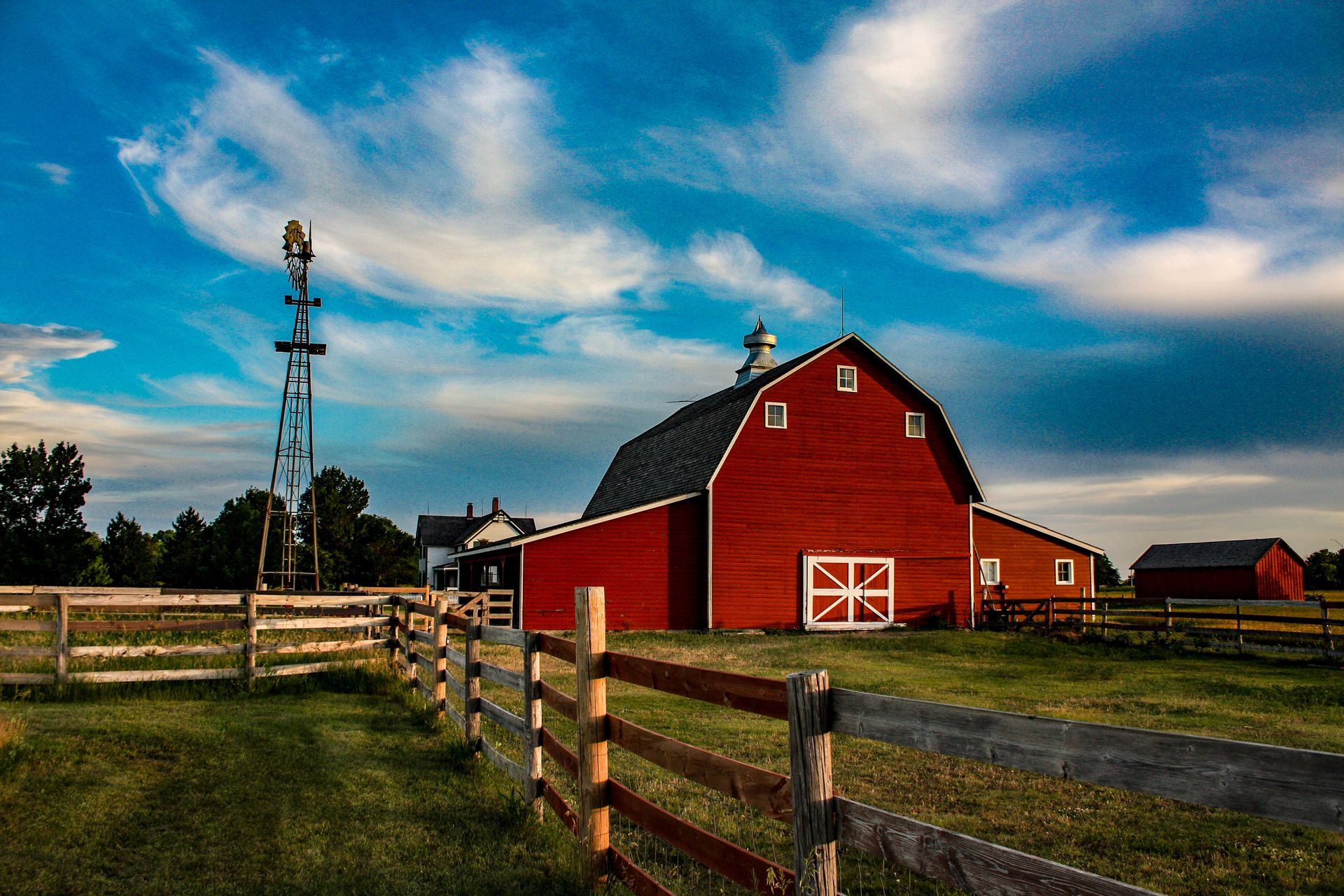 A red barn with a wooden fence and a windmill in the background.