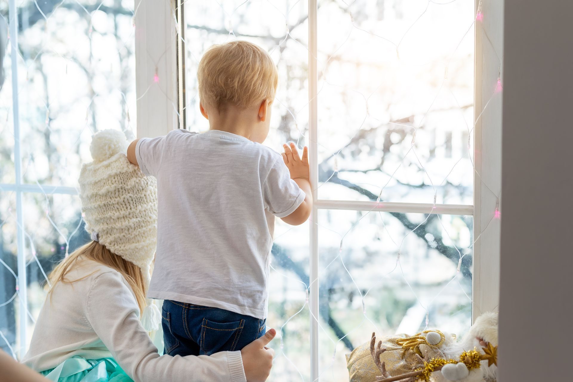 A little boy and a little girl are looking out of a window.