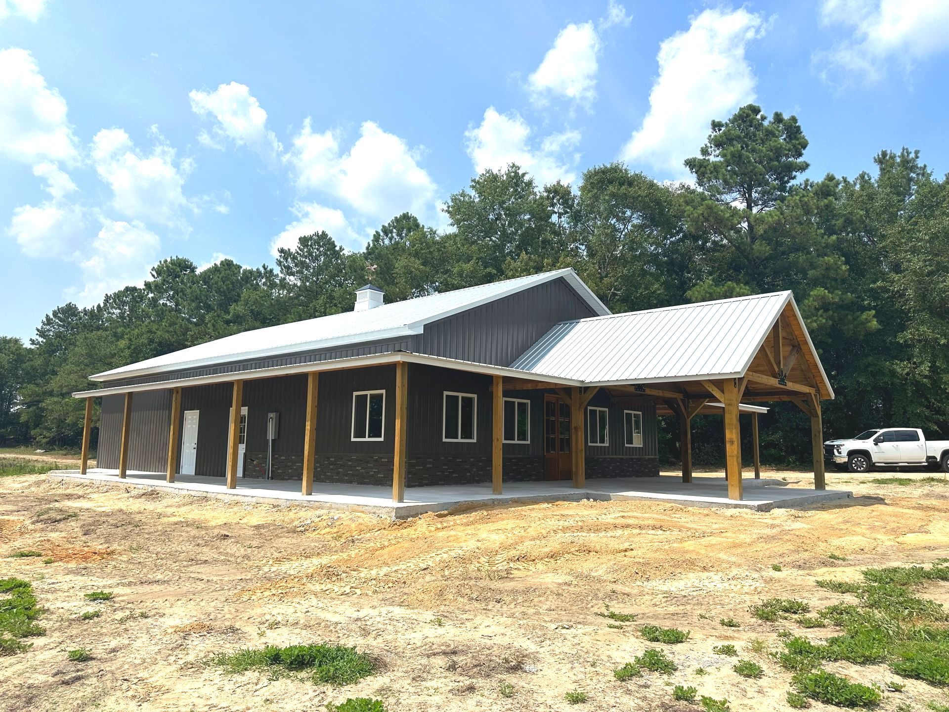 A large barn with a white roof is sitting in the middle of a dirt field.
