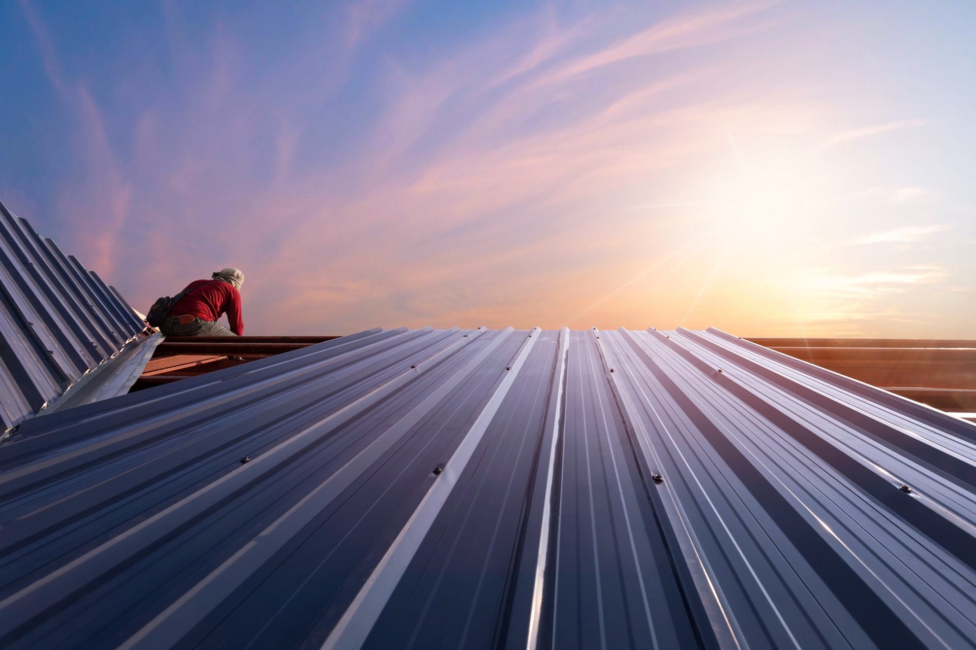 A man is working on a metal roof at sunset.