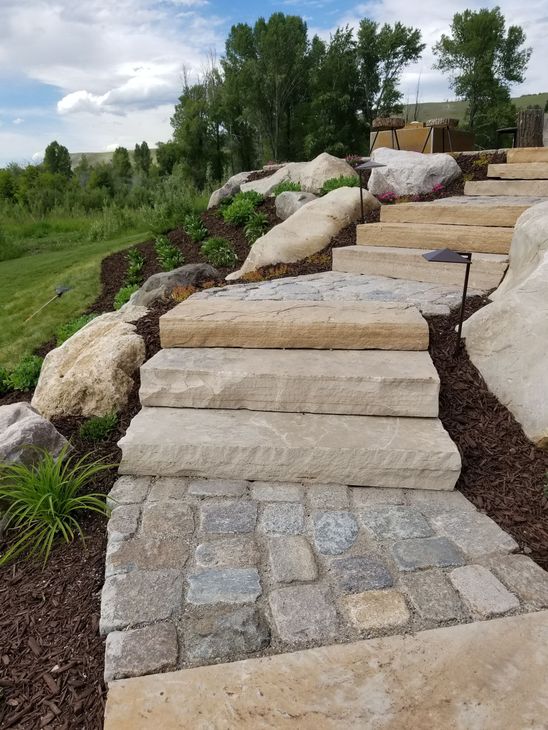 Stone steps leading up a landscaped hill with boulders and greenery under a cloudy sky.