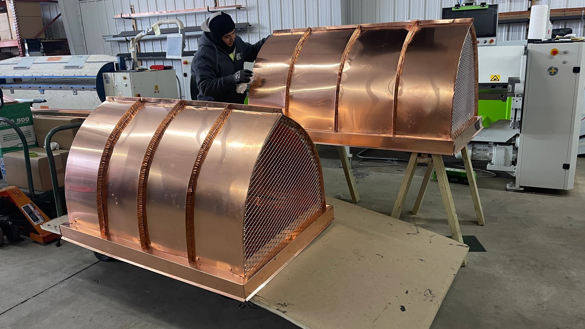 Copper-colored industrial machine parts in a workshop, with a worker in the background.