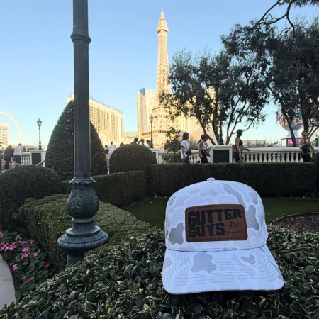 White “Gutter Guys” cap in foreground at a landscaped plaza with Eiffel Tower replica and people in the distance