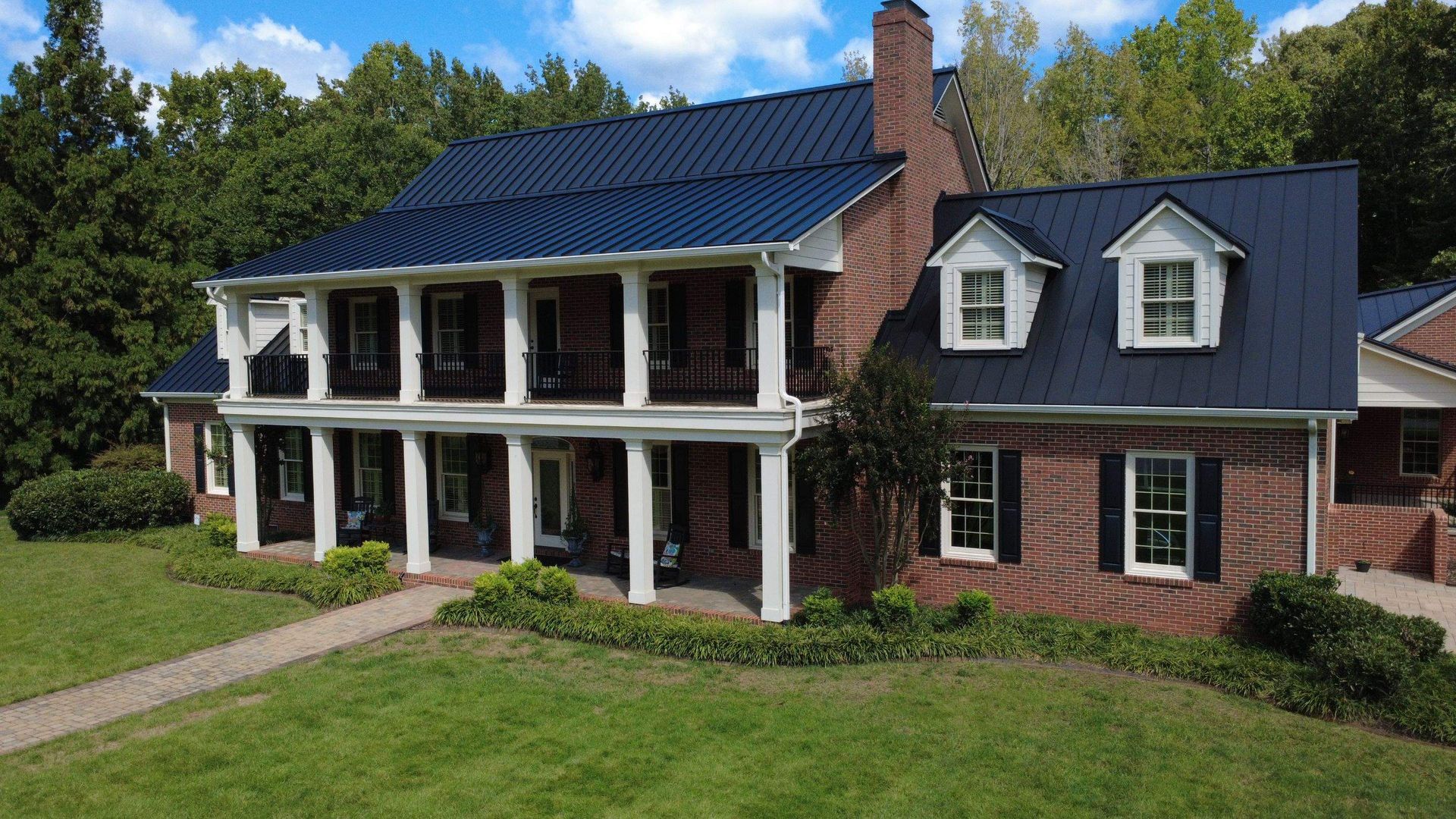 Large brick house with blue roof and white columns, surrounded by trees and a grassy lawn