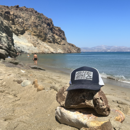 Rocky beach scene with a dark cap resting on a stone in the foreground and a swimmer in the distance.