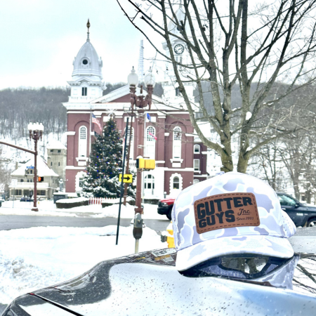 Snowy street with a red brick church and a white hard hat labeled “Gutter Guys” in the foreground