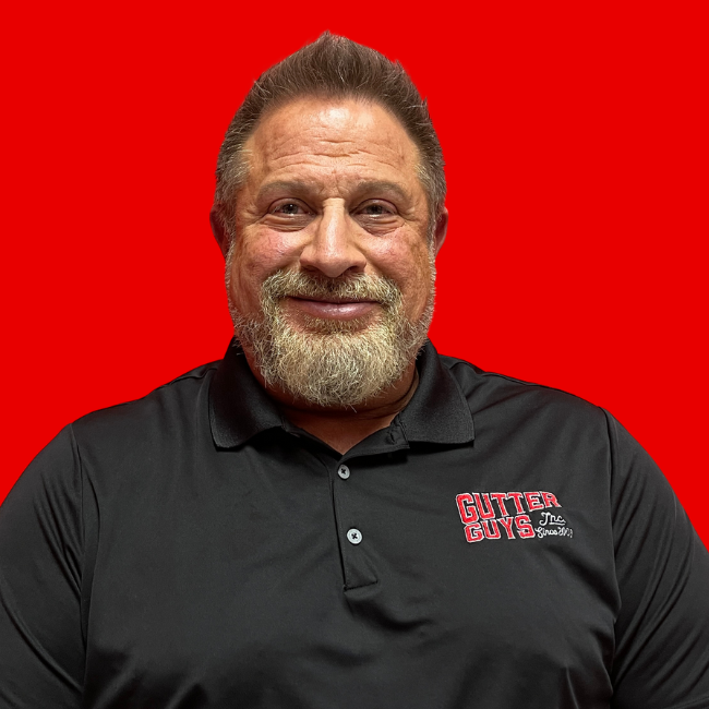Smiling man in black polo shirt with logo, standing against a bright red background.
