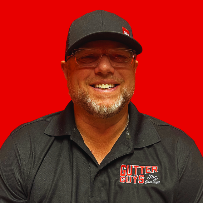 Smiling man in a black cap and polo with Gutter Guys logo against a bright red background