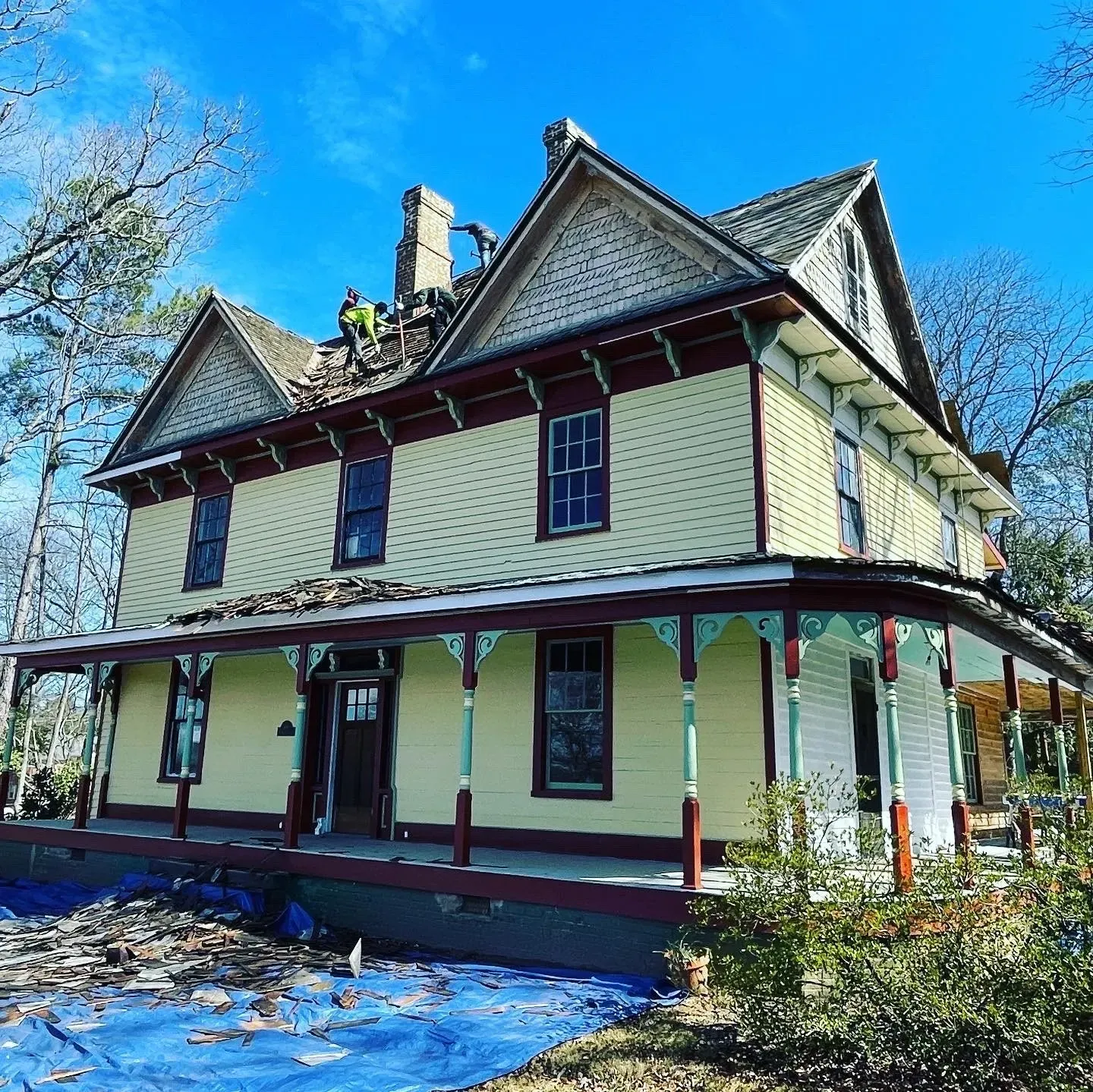 A large yellow house with a porch is being remodeled.