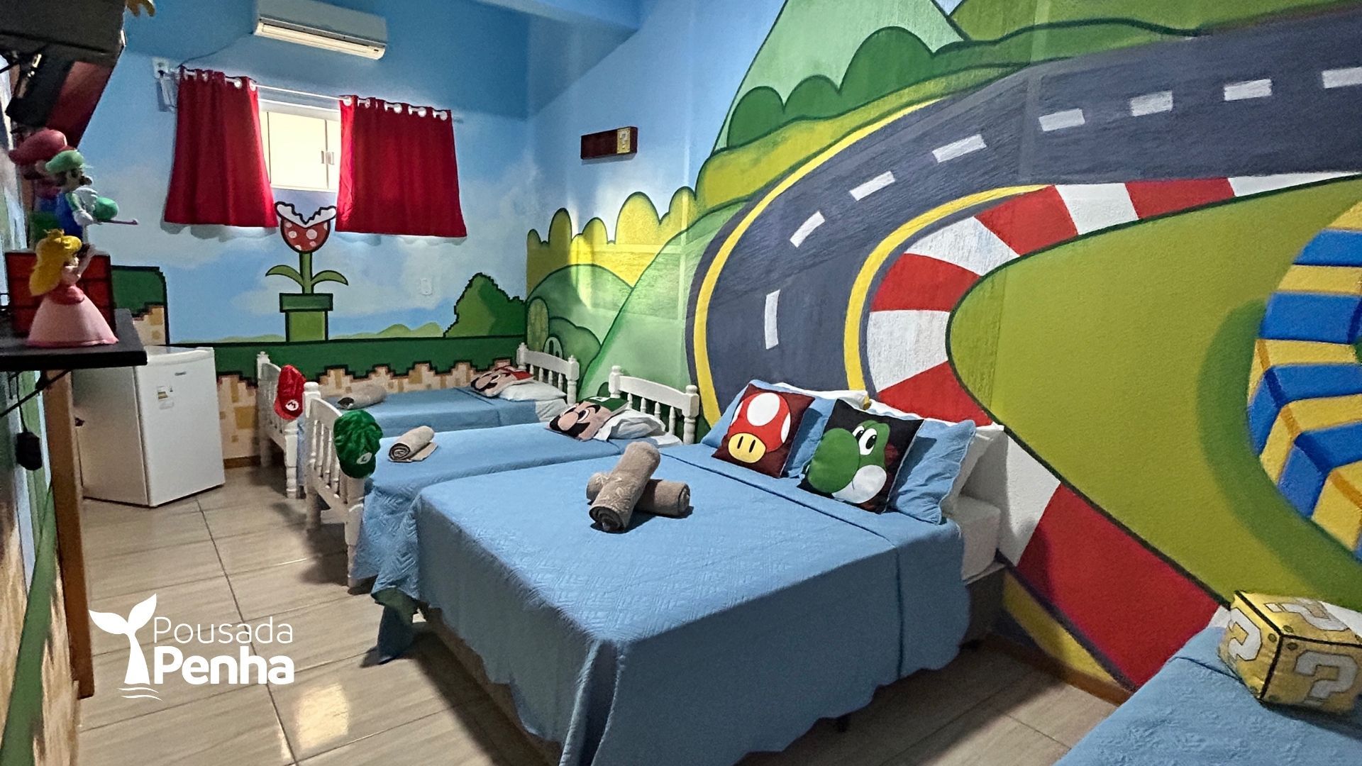 Quarto azul com mural de corrida, duas camas de solteiro, cortinas vermelhas e carrinhos de brinquedo no chão.