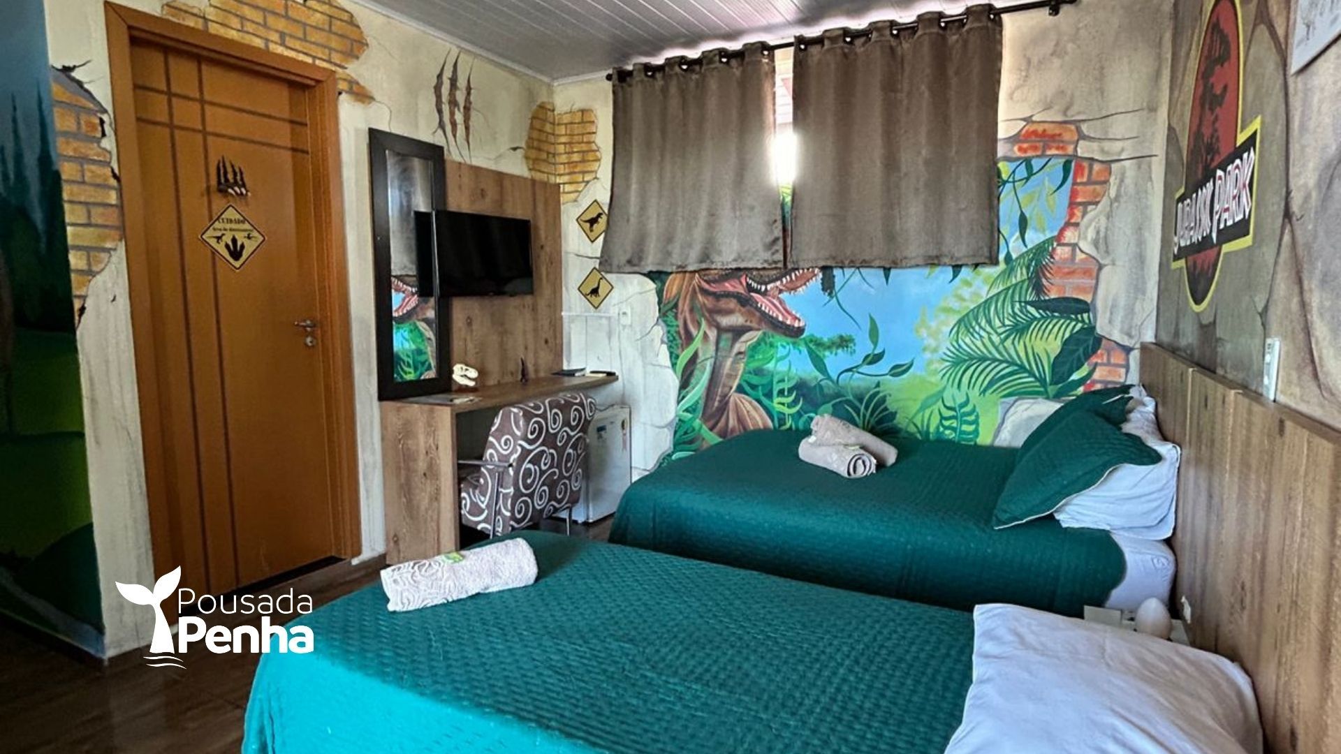 Quarto pequeno com duas camas verdes, TV, cabeceira colorida com mural e janela com cortina.