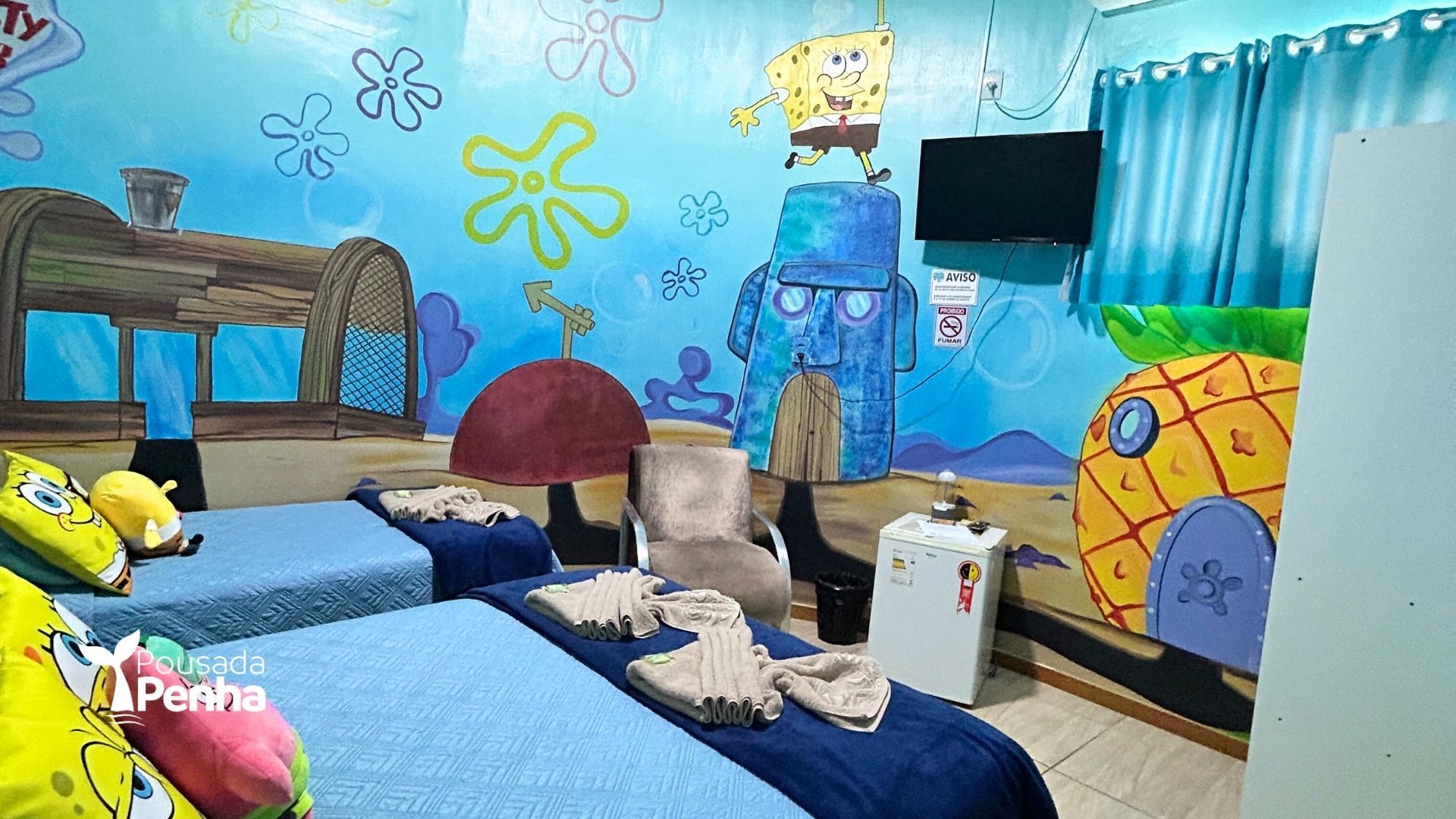 Quarto com tema de desenho animado, com cama azul, decoração do Bob Esponja e paredes com mural do oceano.
