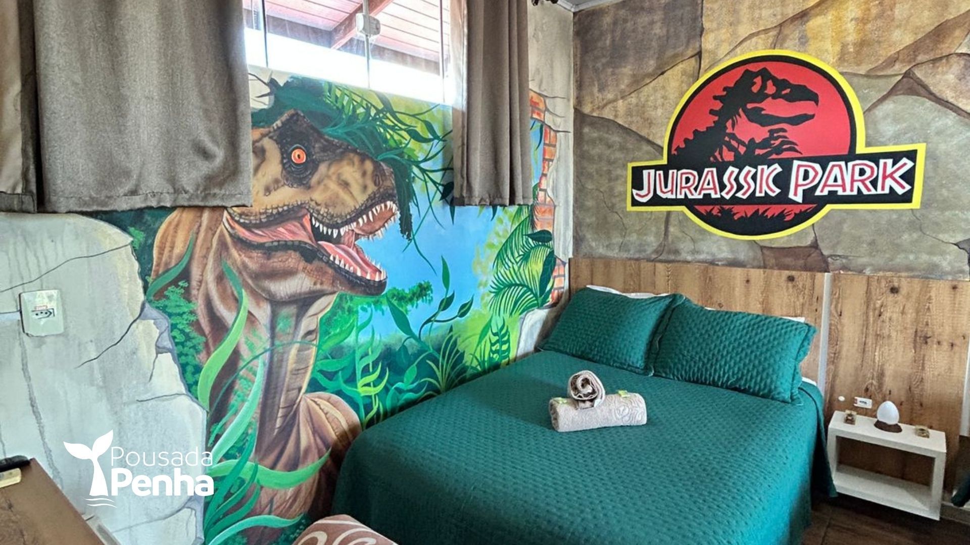 Quarto temático de Jurassic Park com cama verde, mural de dinossauros e placa com o logotipo na parede de madeira.