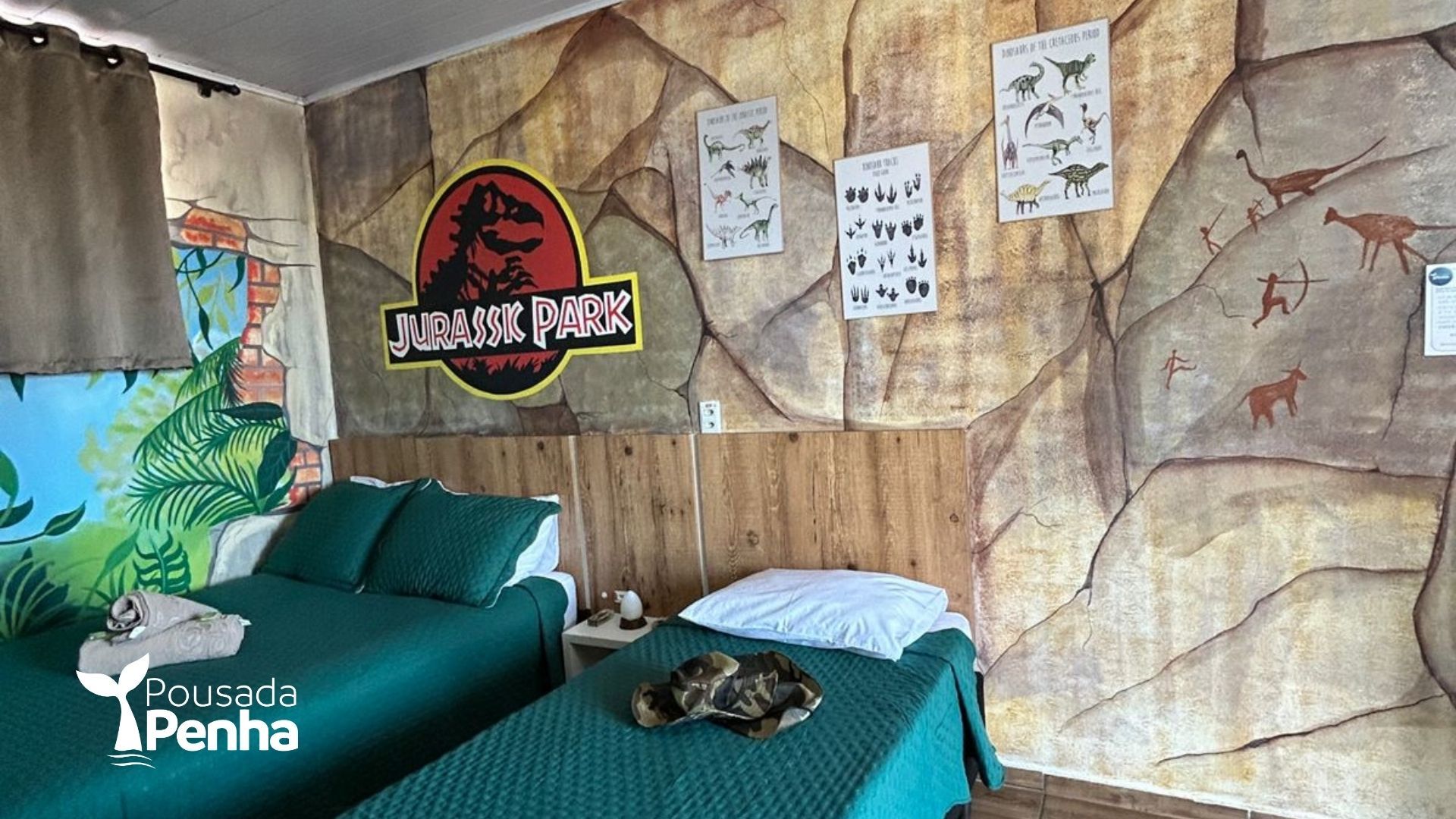 Quarto temático de Jurassic Park com roupa de cama azul-turquesa, mural de dinossauros na parede e pôsteres pendurados.