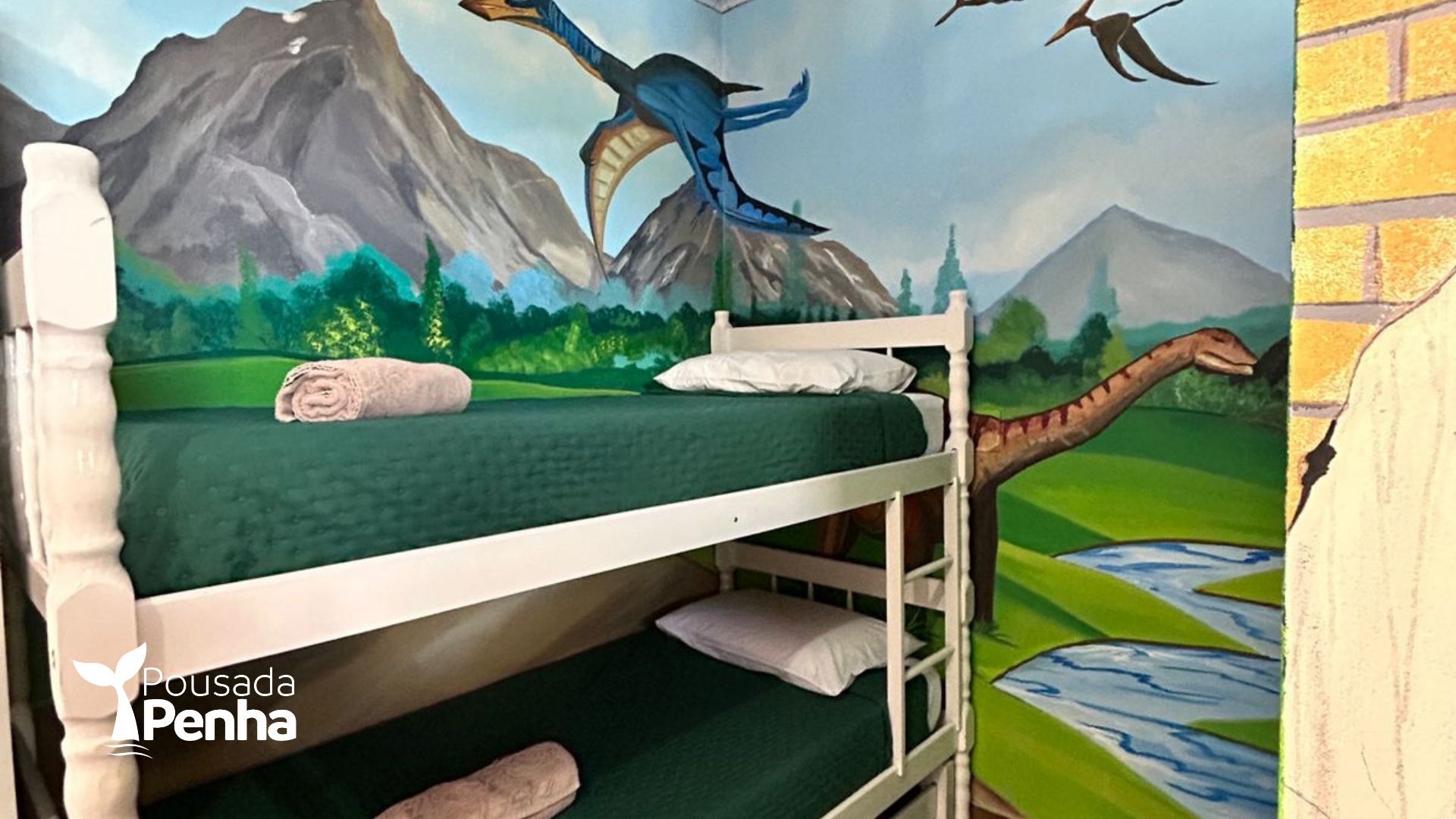 Mural de dinossauros e montanhas atrás de um beliche branco em um quarto colorido.