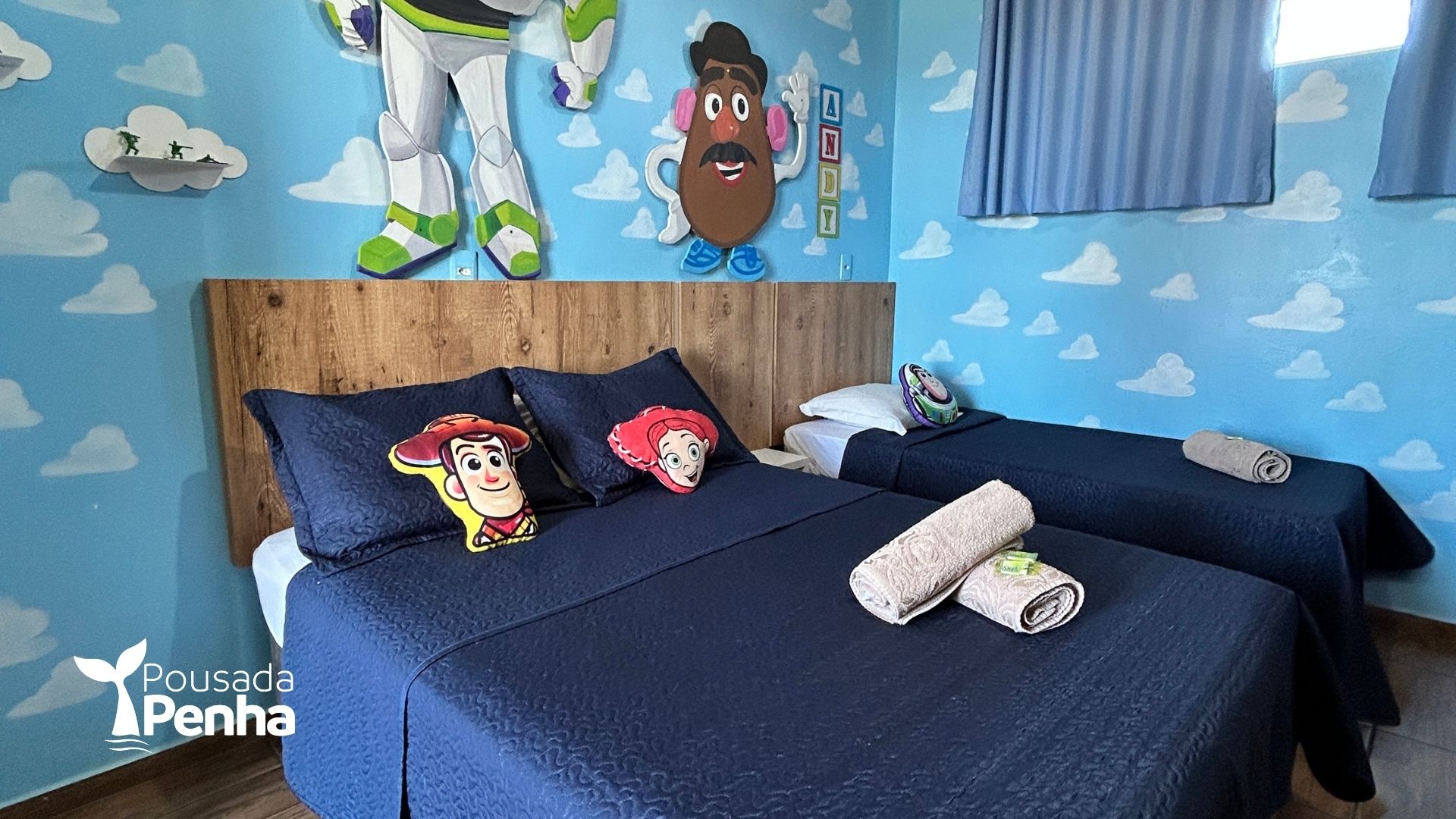 Quarto com tema de brinquedos, com duas camas azul-marinho, adesivos de parede com desenhos animados e cabeceira de madeira.