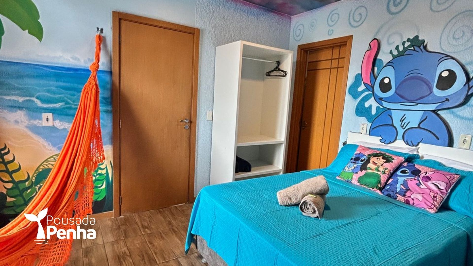 Quarto com colcha turquesa, armário aberto, rede e um grande mural do Stitch na parede.
