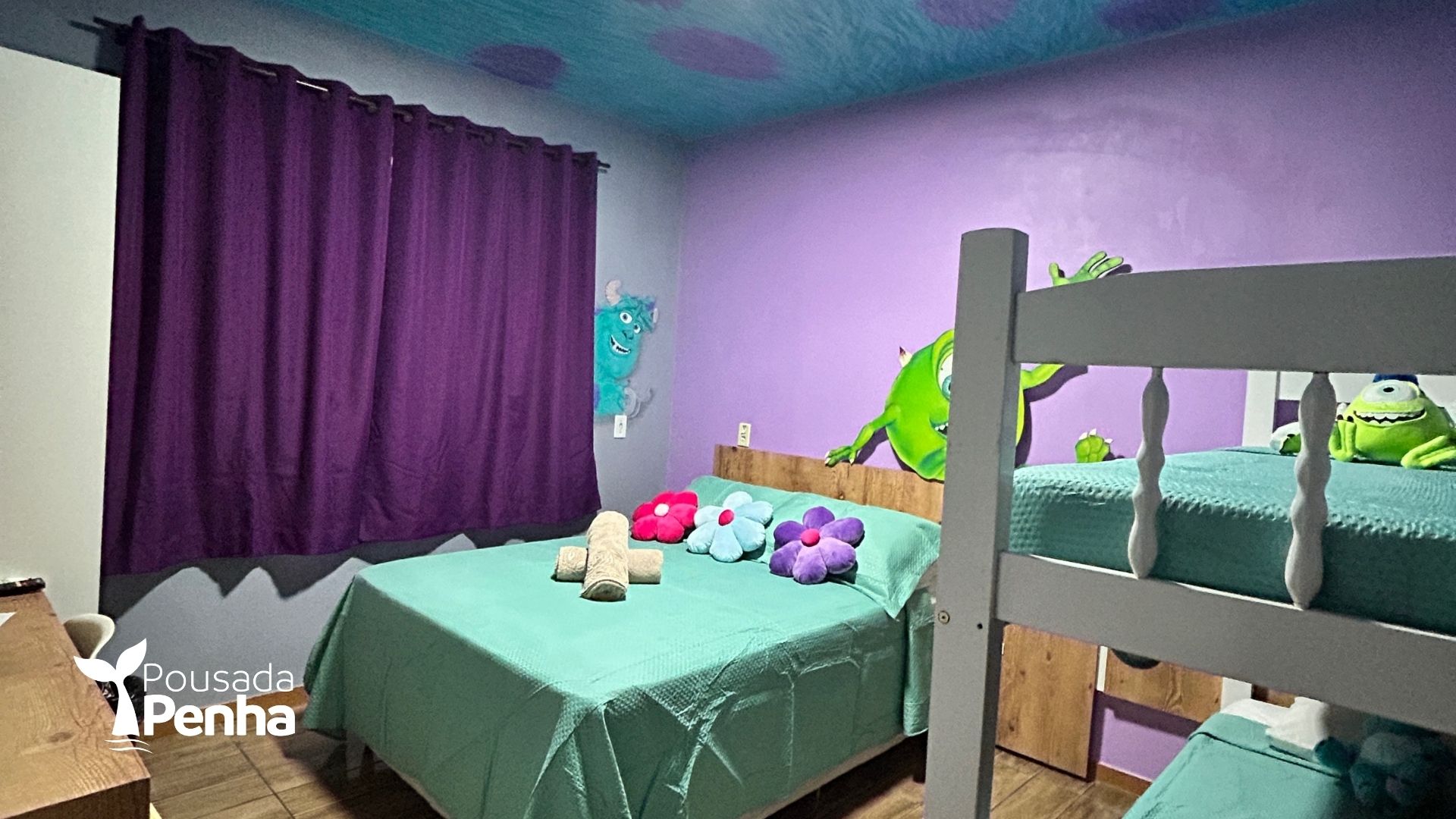 Quarto infantil com cortinas roxas, roupa de cama turquesa e brinquedos na cama.