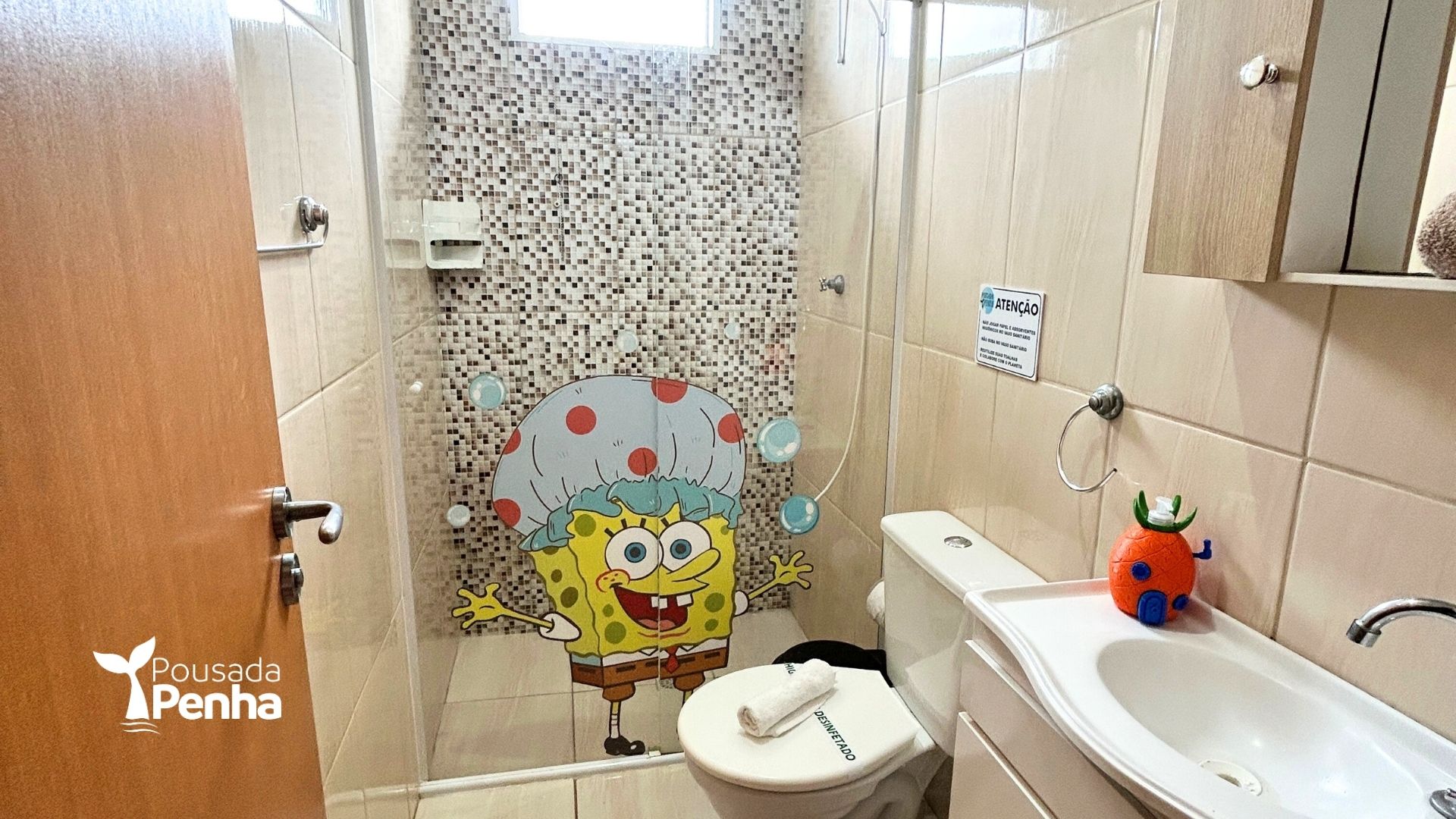 Banheiro pequeno com vaso sanitário, pia e cortina de chuveiro com estampa do Bob Esponja.