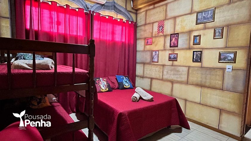 Quarto aconchegante com beliche e cortinas vermelhas, uma cama com toalhas dobradas e fotos emolduradas na parede.