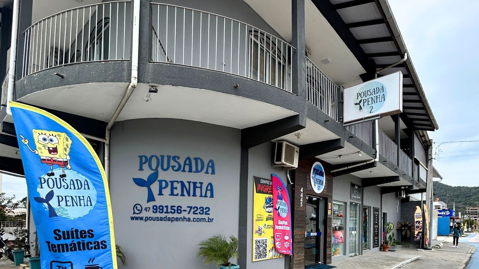 Vista da rua da entrada do hotel Pousada Penha com sinalização azul e varanda externa.