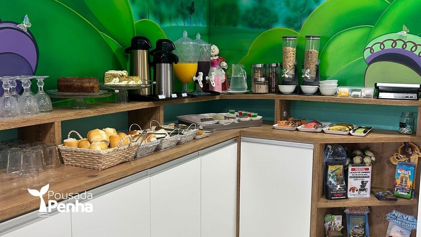 Buffet de café da manhã com frutas, pães, café e doces em um balcão contra uma parede com um mural verde.