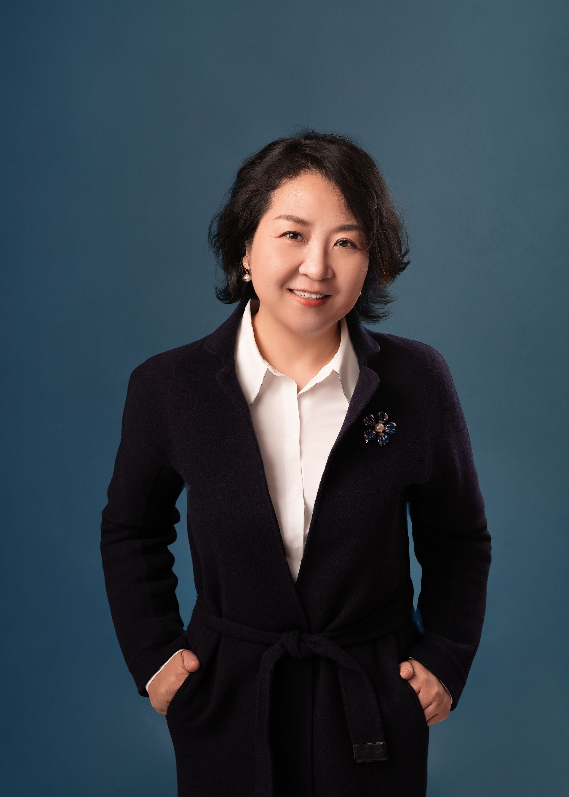 Woman in gray suit with arms crossed, smiling against a white background.