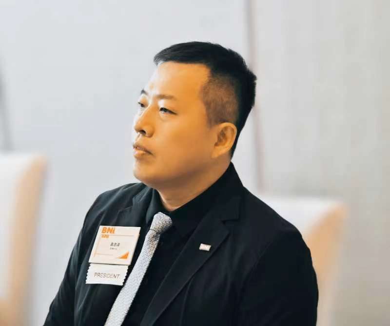 Woman in a grey business suit, arms crossed, smiles at the camera against a white background.