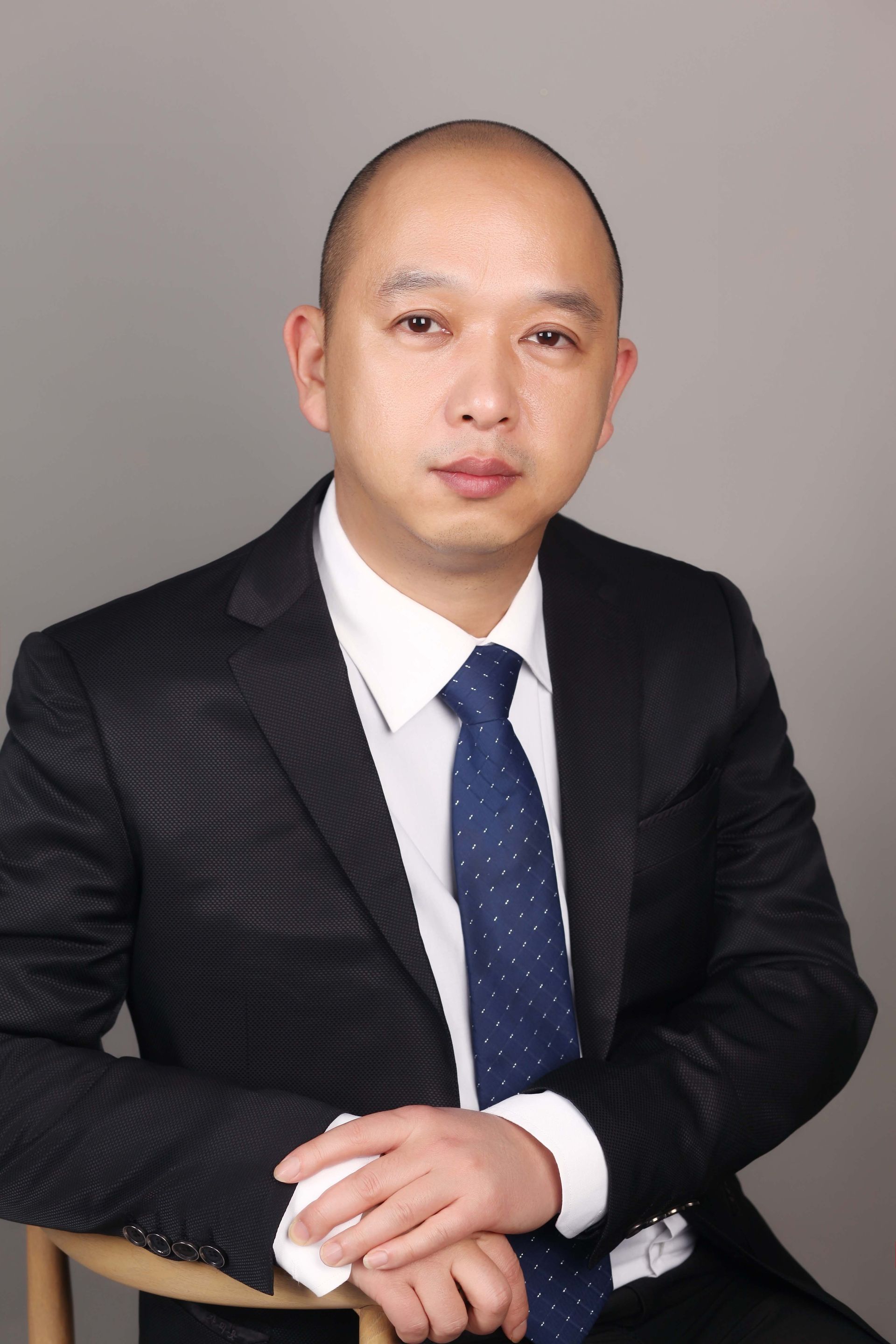 Man in a suit and tie, sitting on a chair, looking at the camera.
