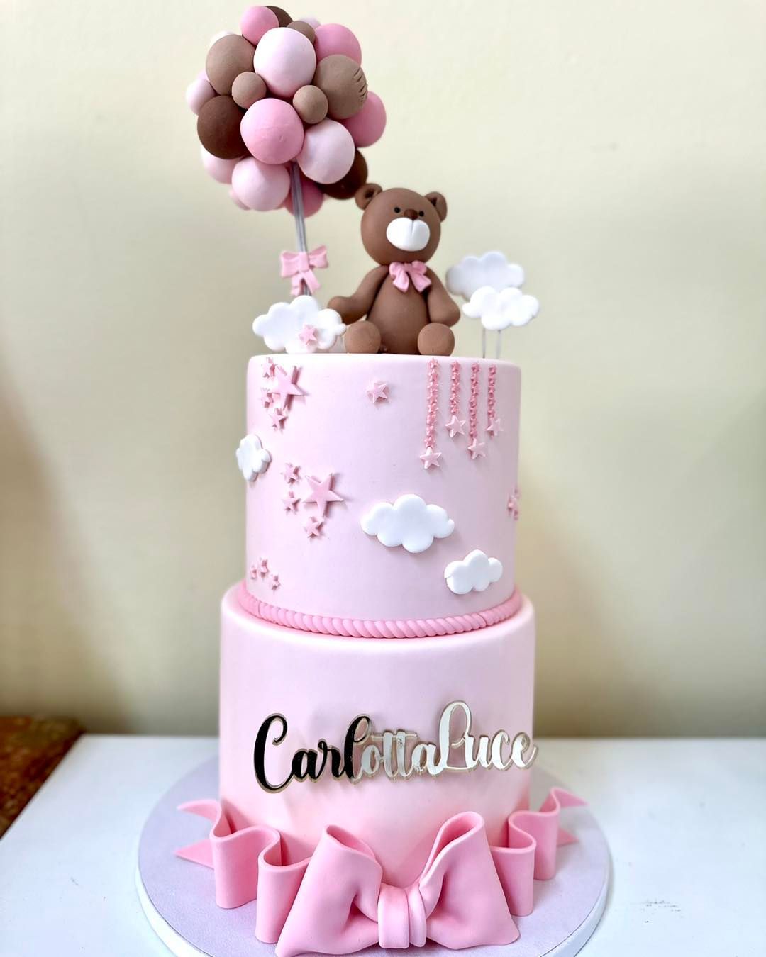 Una torta rosa con un orsacchiotto e dei palloncini sopra.