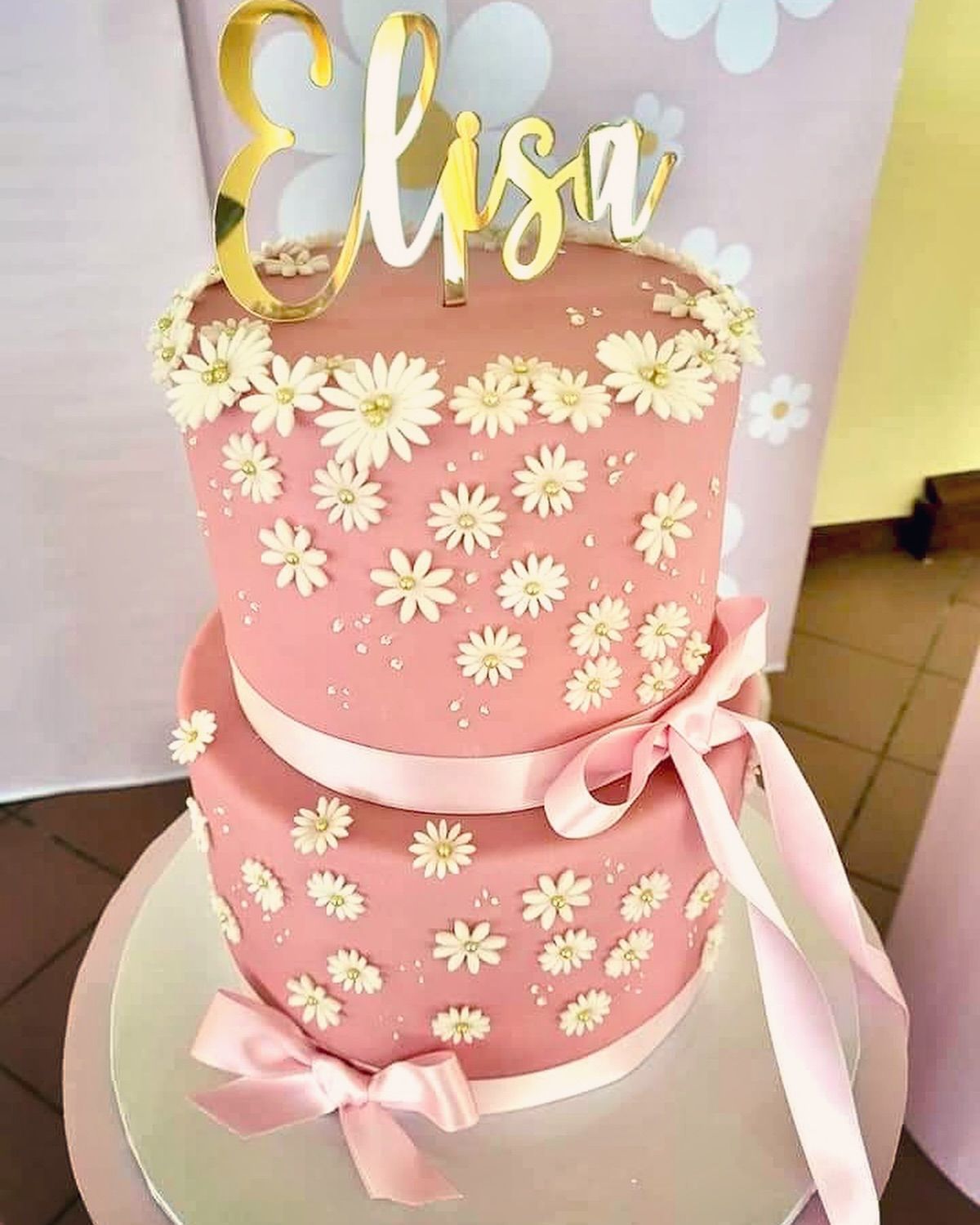 Una torta rosa con margherite bianche e il nome elisa sopra
