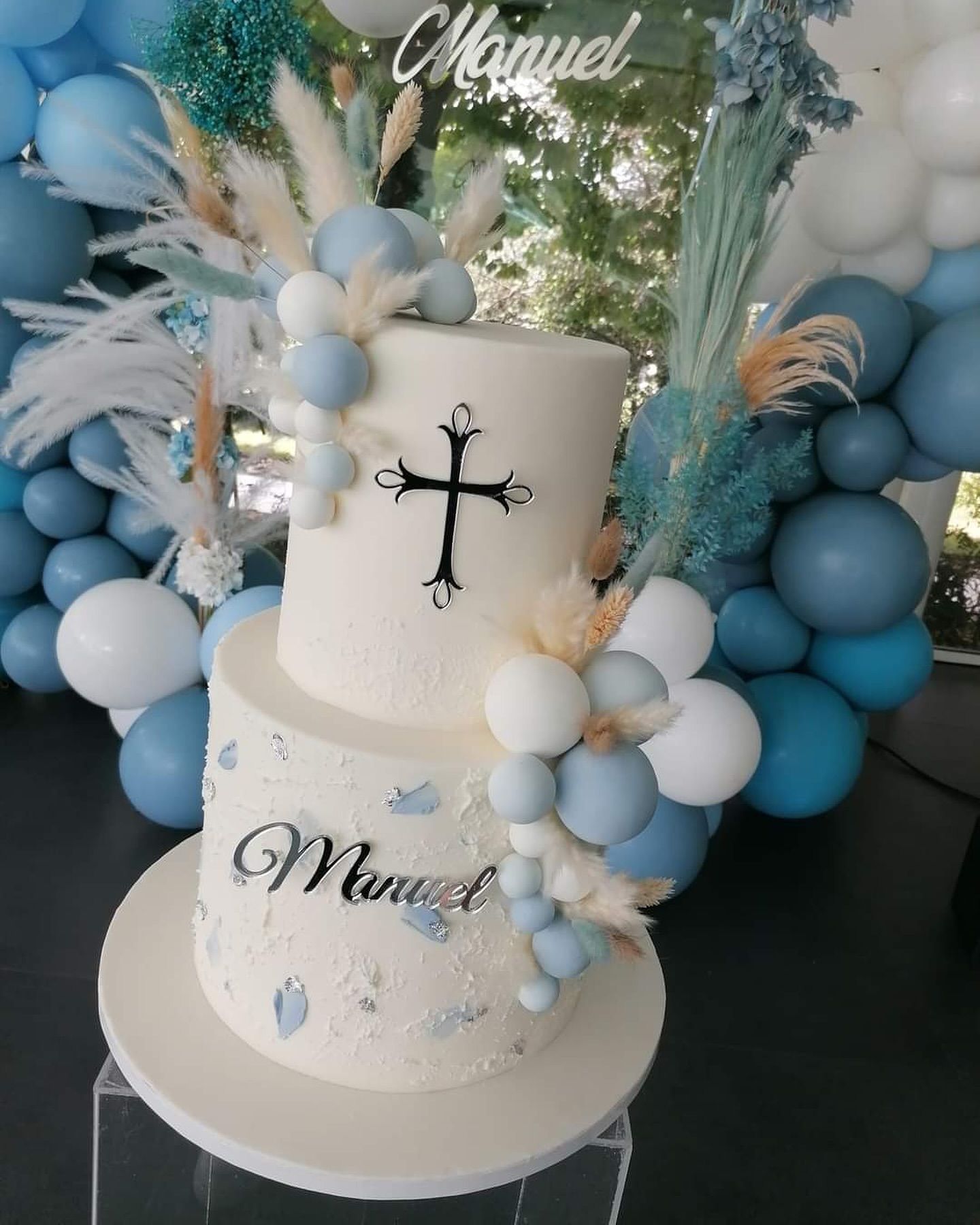 Una torta bianca con una croce in cima è circondata da palloncini blu.