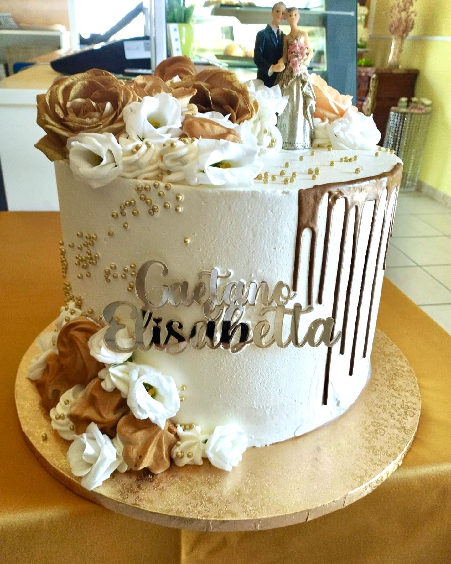 Una torta bianca con fiori dorati e il nome isabella sopra