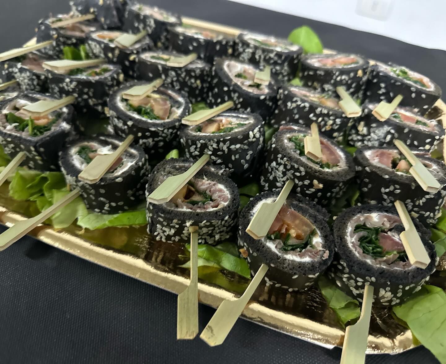 Un vassoio di rotoli di sushi nero con stuzzicadenti su un tavolo.