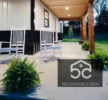 White rocking chairs on a covered porch with ferns, green lawn, and a construction company logo.