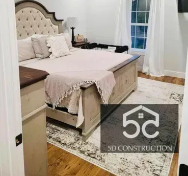 Bedroom with large bed, rug, window, and wooden floors. Neutral tones.