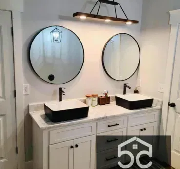 Bathroom with two black sinks, round mirrors, and a wooden light fixture.