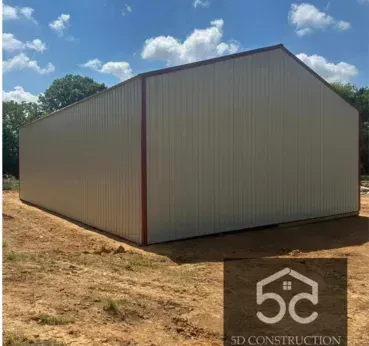 A large, metal building with a red trim on a dirt lot under a blue sky. Logo for 5D Construction in the corner.