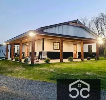 Modern, black and white house with porch. Green yard, gravel driveway, and logo in the corner.