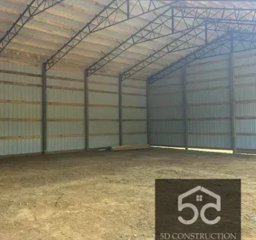 Inside of a newly constructed, empty metal building with a dirt floor and a 5C Construction logo.