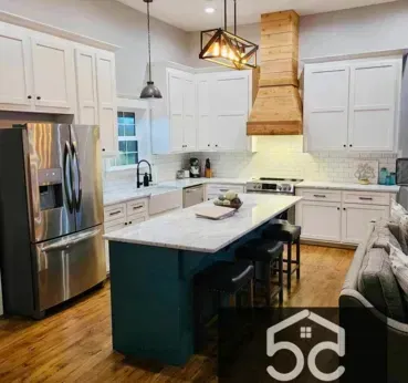 Kitchen remodel with white cabinets, teal island, wooden range hood, and stainless steel appliances.