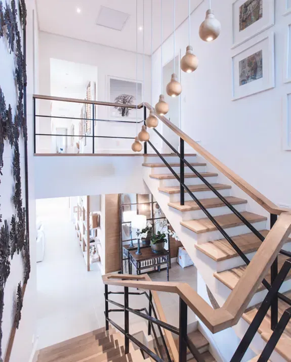 Staircase with light wooden steps, black metal railings, and pendant lights. White walls, framed artwork, and second-floor