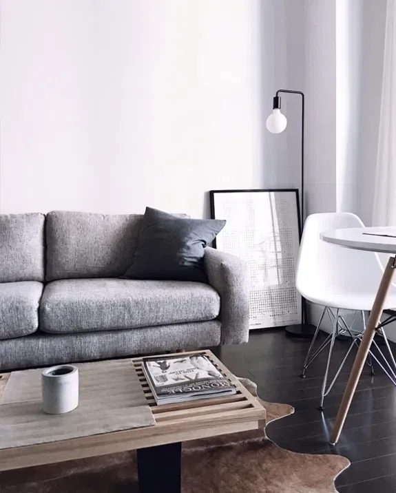 Cozy living room with gray sofa, white table and chair, black framed art, and floor lamp.